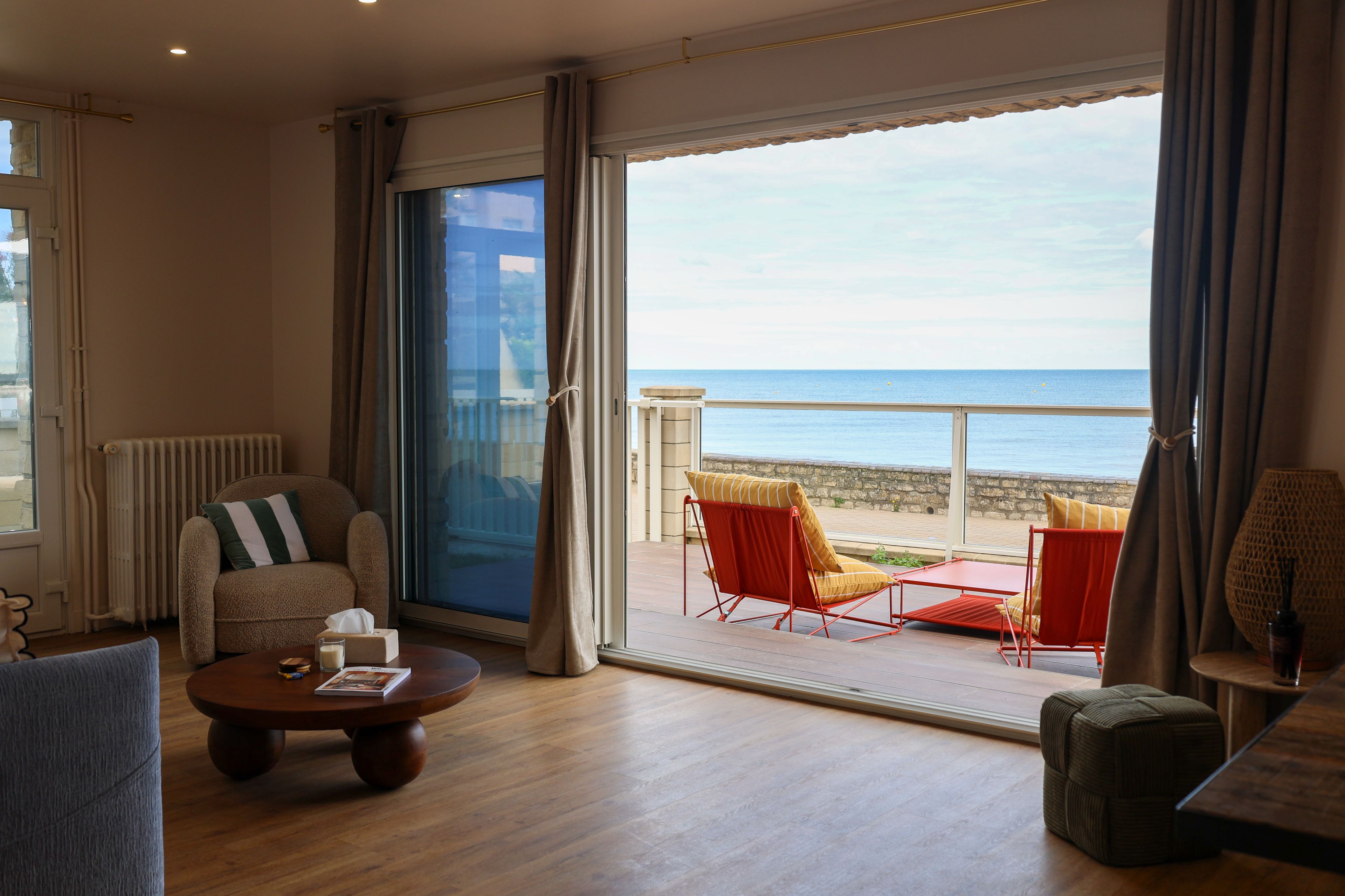 Un salón amplio con un gran ventanal corredera que da a un balcón con vistas al mar.