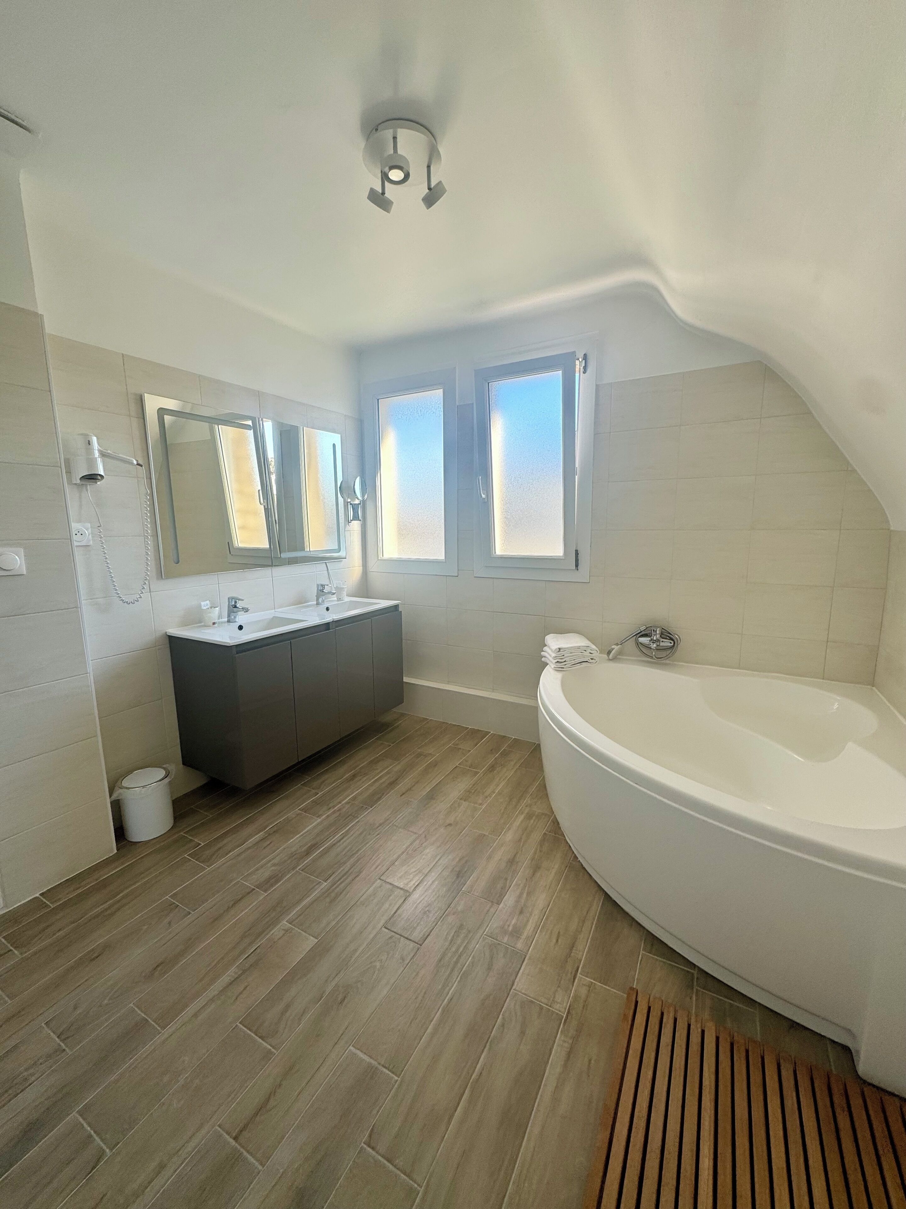 Un baño moderno con una bañera independiente, un tocador con lavamanos dobles y un espejo grande sobre el tocador.