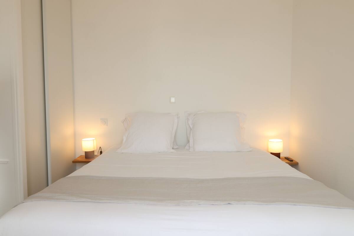 A neatly made bed with white linens, two bedside lamps, and a wooden nightstand.