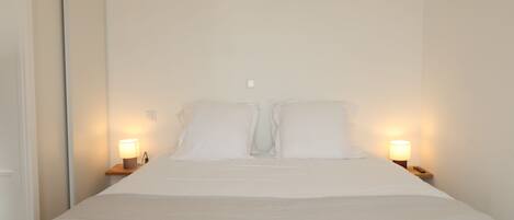 A neatly made bed with white linens, two bedside lamps, and a wooden nightstand.