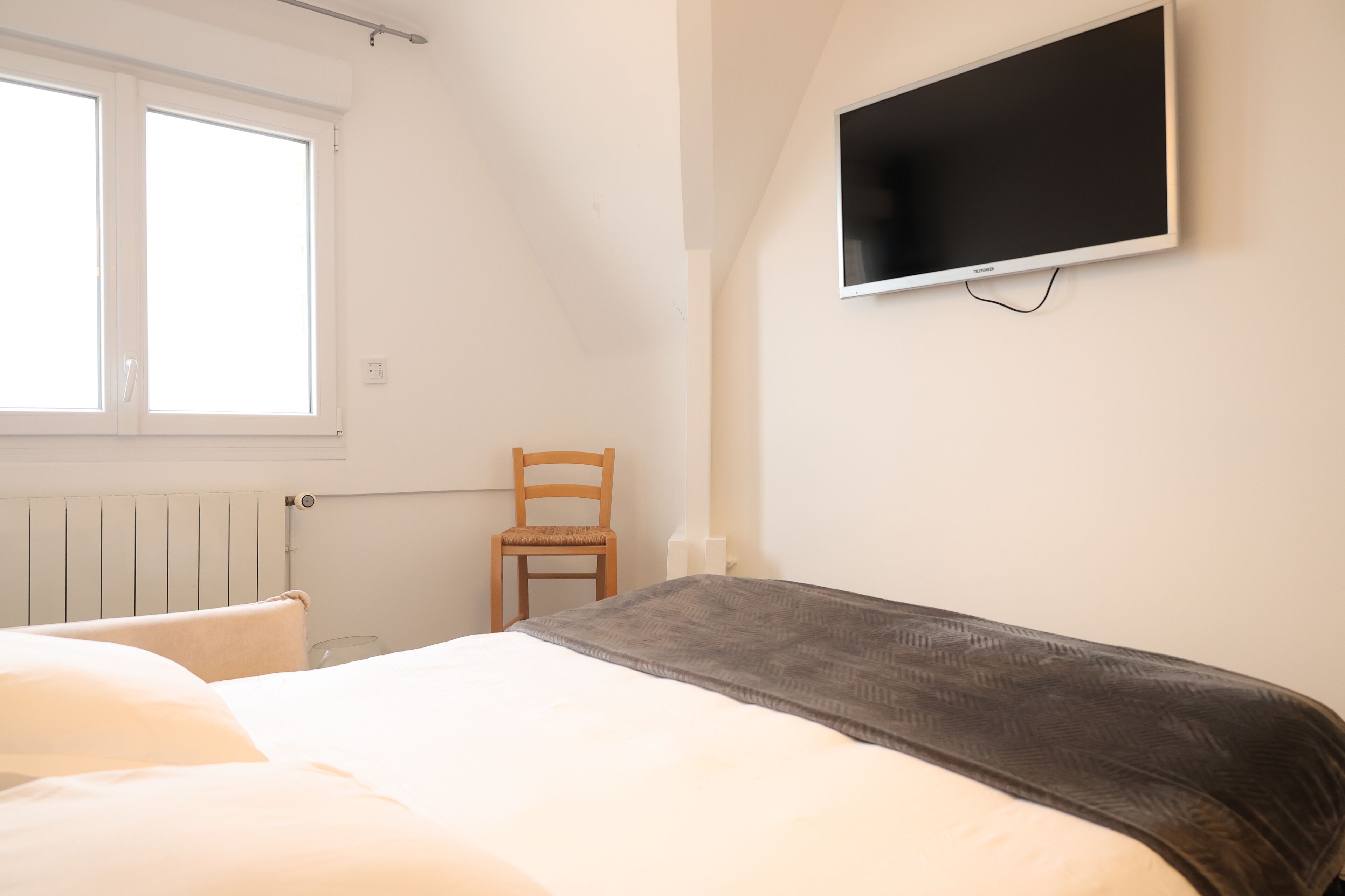 Une chambre à coucher avec un lit, une chaise, un téléviseur fixé au mur et une fenêtre.