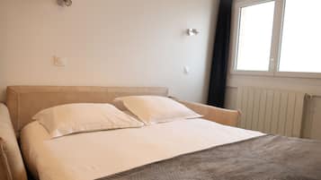A bedroom with a bed, two pillows, a headboard, a window, and a radiator.