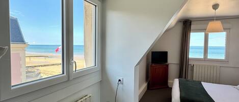 Habitación de hotel con una cama, una mesita con lámpara, un radiador y vistas a la playa.