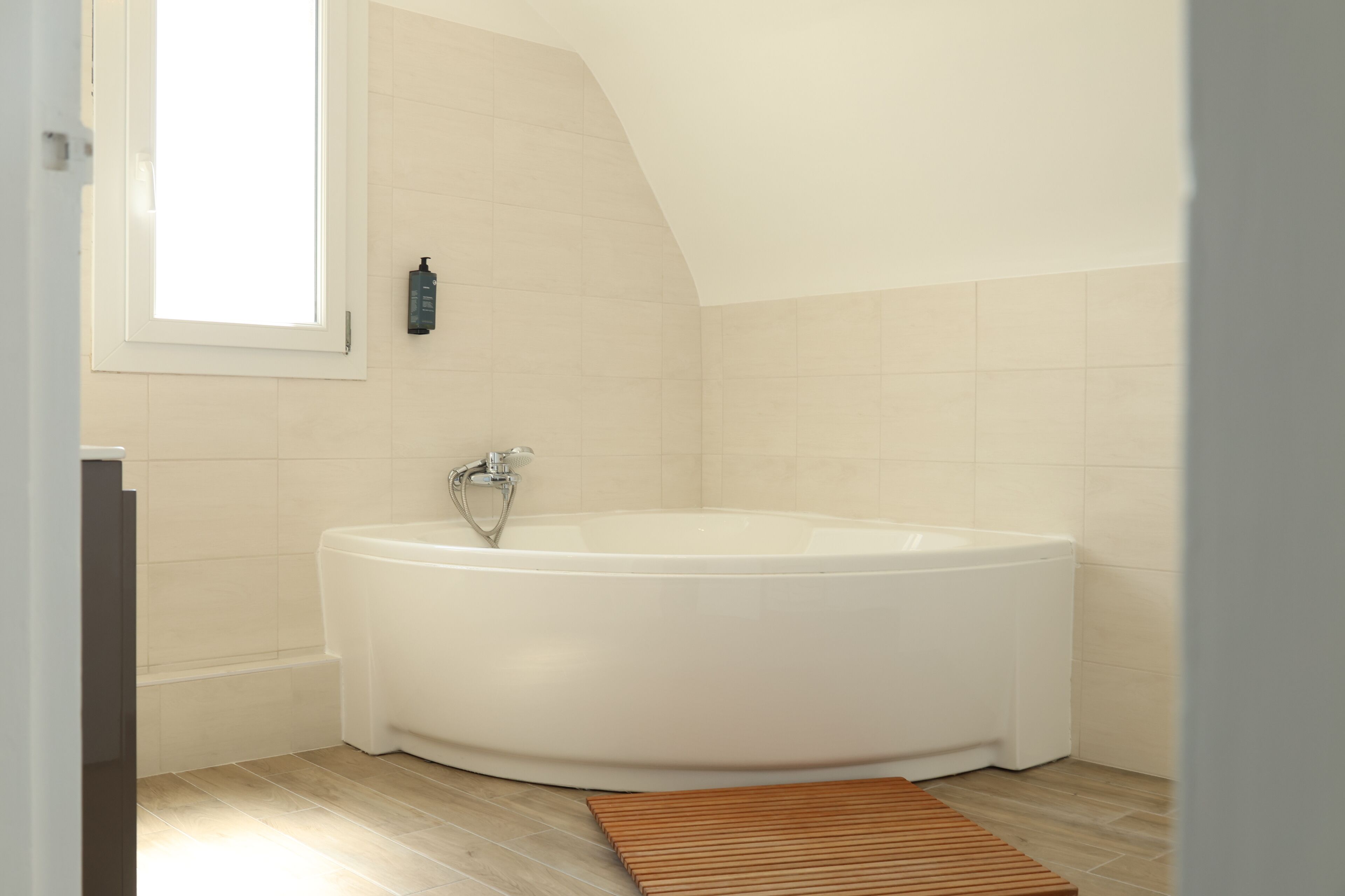 A modern bathroom with a freestanding bathtub, a window, and a wooden mat on the floor.