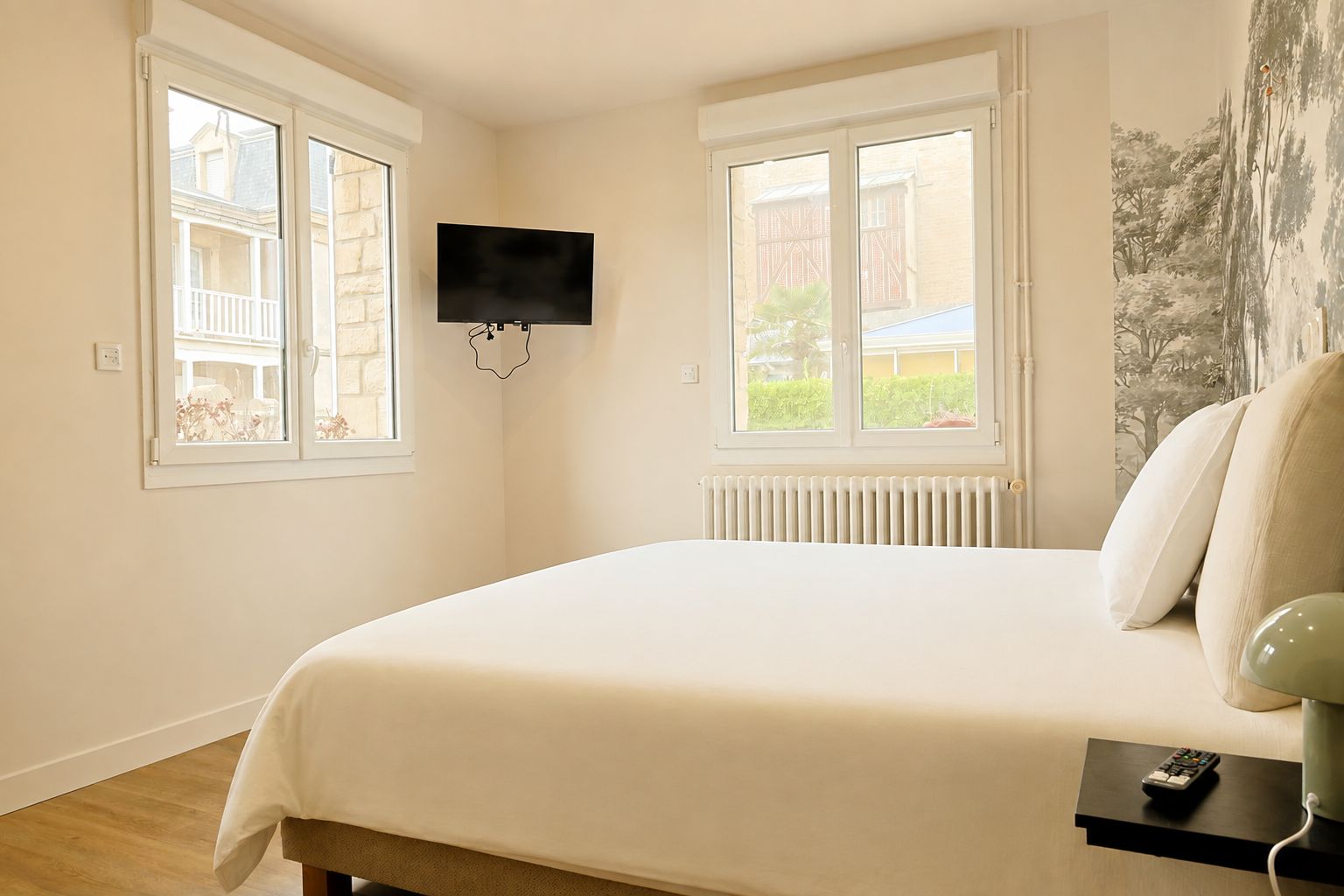 A bedroom with a bed, a TV mounted on the wall, and a window with a view of buildings.