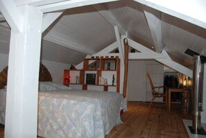 Cozy attic bedroom with a large bed, wooden shelf, and comfortable chair.