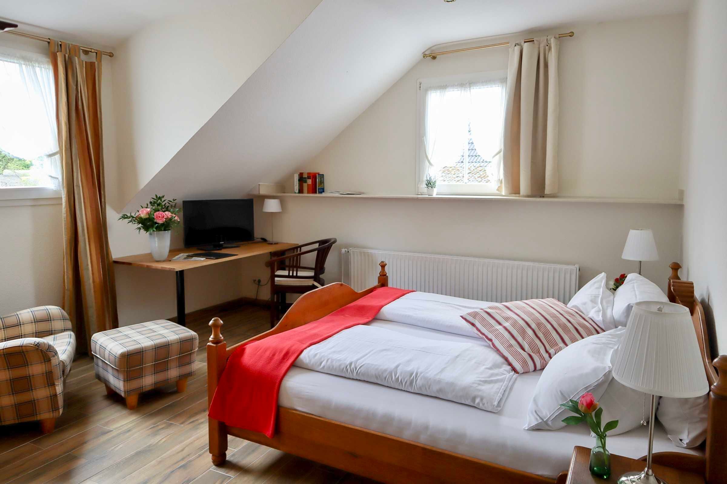 A bedroom with a bed, a desk, a chair, a TV, and a window with curtains.