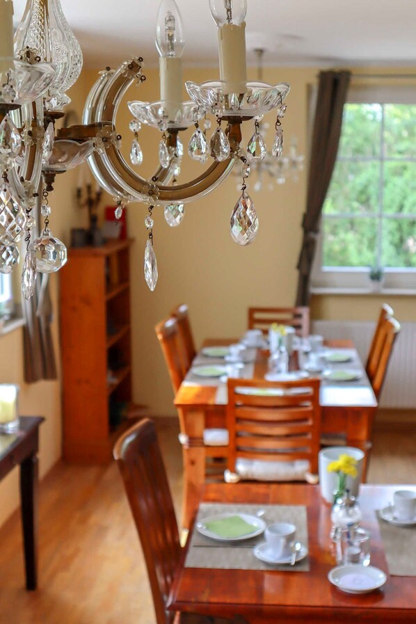 A dining area with a wooden table set for four, surrounded by chairs. A chandelier with crystal decorations hangs above.