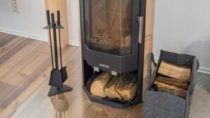A modern wood-burning stove with a glass door, a log storage box, and a black chimney. - Ferienhaus Harzblüte (Blankenburg (Harz))