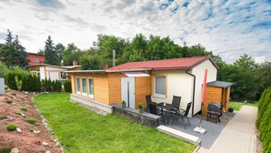 A small, single-story house with a red-tiled roof, a patio with outdoor furniture, and a well-maintained lawn. - Ferienhaus Harzblüte (Blankenburg (Harz))