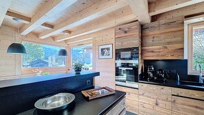 A modern kitchen with wooden paneling, a black countertop, and a view of the outdoors. - Luxurious Duplex Chalet Apartment with Stunning Mont Blanc View (Combloux)