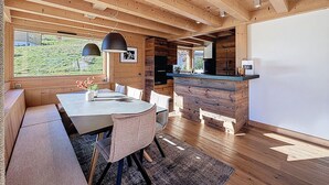A modern kitchen with wooden beams, a dining area with a bench, and a view of a green landscape. - Luxurious Duplex Chalet Apartment with Stunning Mont Blanc View (Combloux)