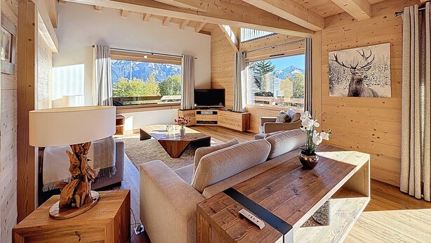 A cozy wooden cabin interior with a sofa, coffee table, and TV. Large windows offer mountain views. - Luxurious Duplex Chalet Apartment with Stunning Mont Blanc View (Combloux)