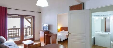 Una habitación de hotel con una mesa de comedor de madera, una cama con ropa de cama blanca, un escritorio con una computadora y un baño con espejo y lavamanos.