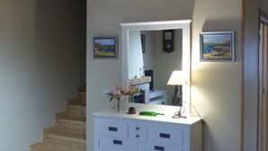 Une pièce avec un escalier en bois, une coiffeuse blanche avec un miroir et un tableau accroché au mur.