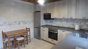 Une cuisine avec des meubles de rangement en bois, un réfrigérateur, un four à micro-ondes, un évier et une table à manger avec des chaises.