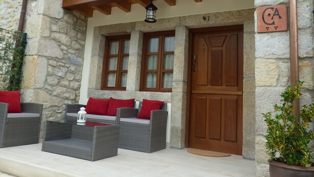 Un bâtiment en pierre doté d’un balcon en bois, d’une porte et d’un espace extérieur aménagé avec des coussins rouges.