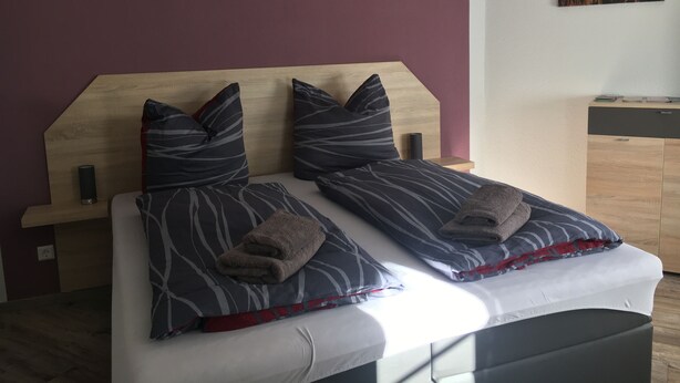 Ein Bett mit Holz-Kopfteil, zwei Kissen und einem gefalteten Handtuch.