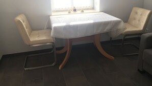 Ein kleiner Essbereich mit einem Tisch, zwei Stühlen, einem Fenster mit Blick und einem Fliesenboden.