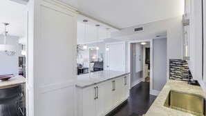 A modern kitchen with white cabinetry, a marble countertop, and pendant lighting. - Wing Beachfront Condo | Pool, Gym & Tennis Courts (Marco Island)