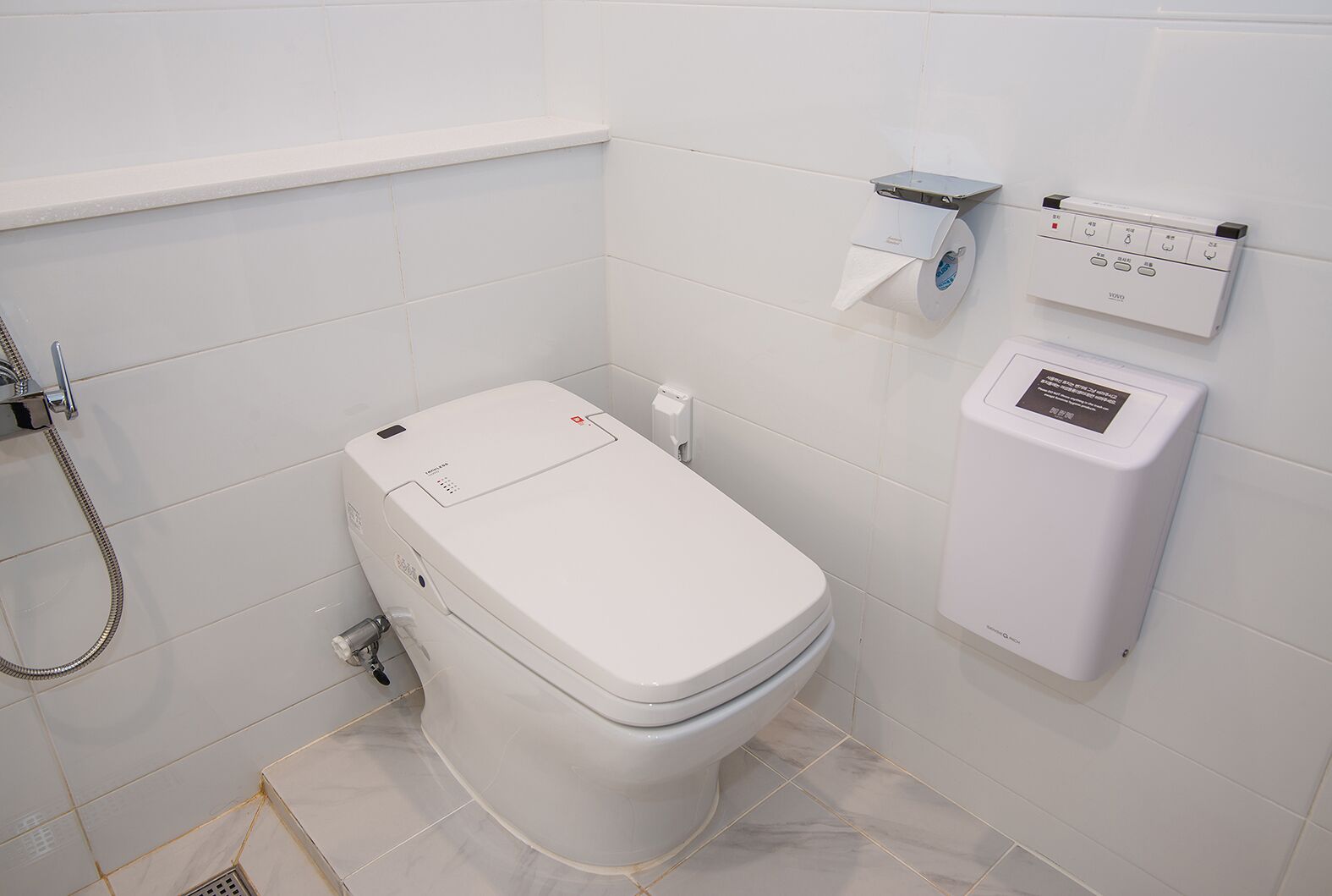 Un baño moderno con inodoro, ducha y dispensador de papel higiénico en la pared.