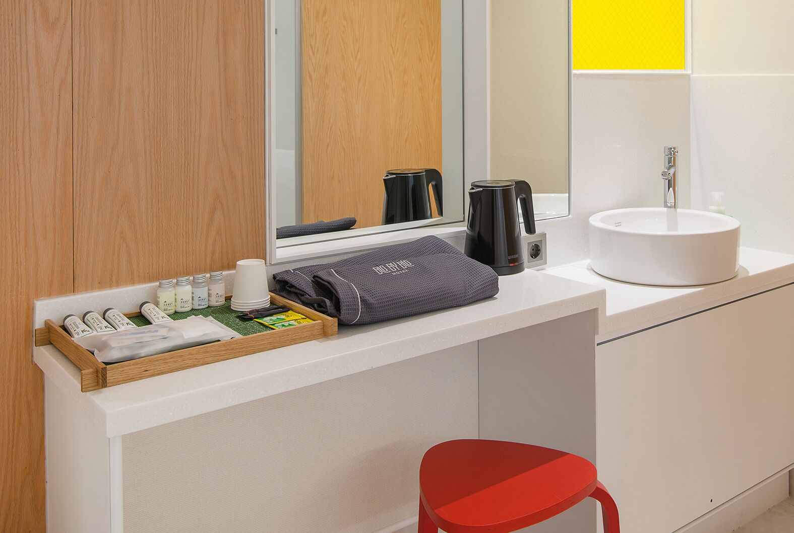 A modern bathroom with a wooden vanity, a white sink, a mirror, and a red chair.