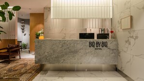 Una moderna zona de recepción de hotel con mostrador de mármol, un ventanal grande y una decoración minimalista.