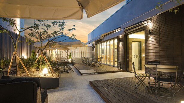 Un área de patio al aire libre con piso de madera, mesas, sillas y sombrillas.