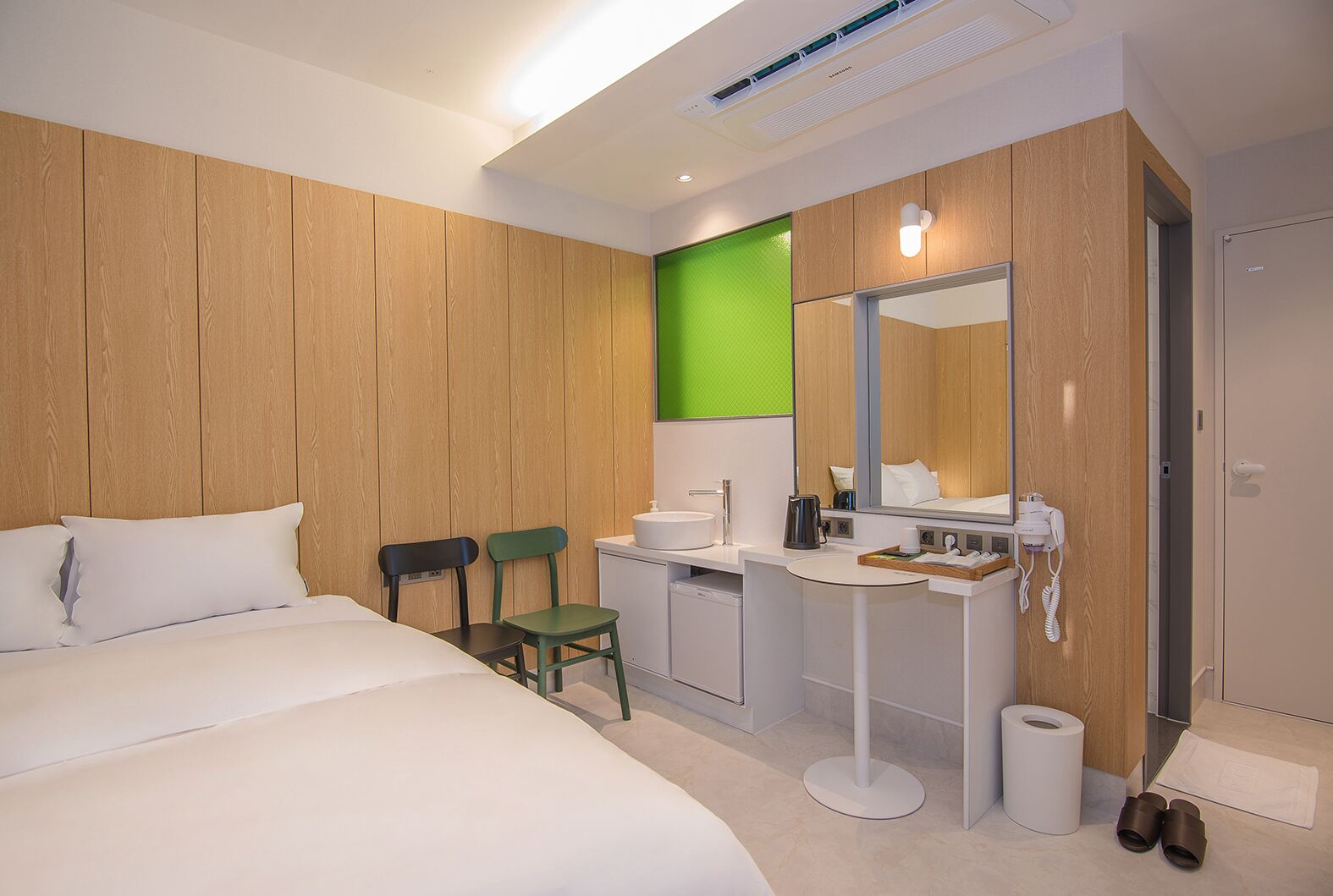 Una habitación de hotel moderna con una cama grande, un escritorio con lavabo, un espejo y una pared de acento verde.