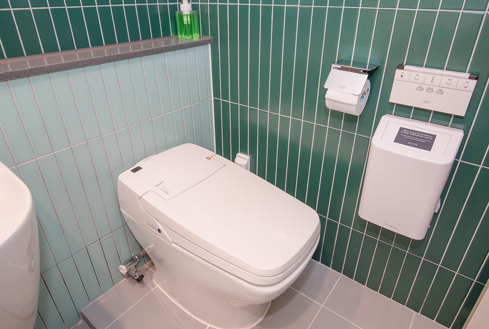 Un baño con inodoro, secamanos automático y dispensador de toallas de papel.
