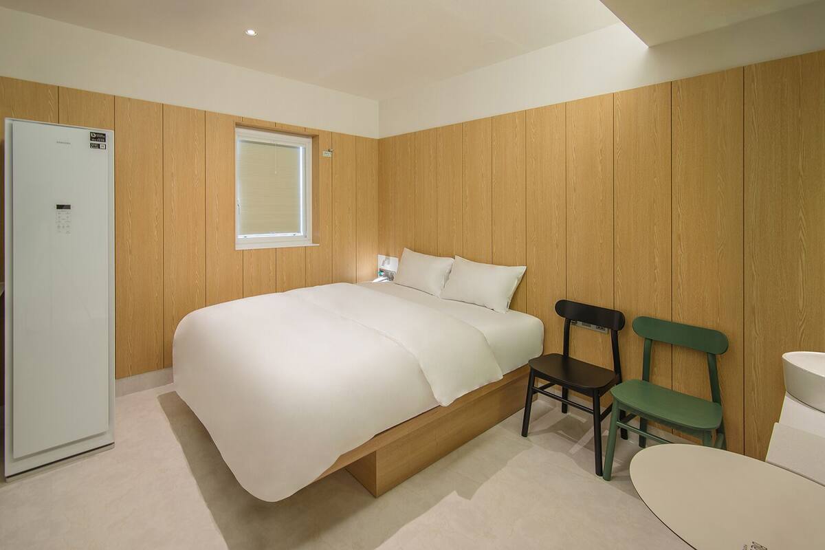 Un dormitorio con cama, armario de madera, ventana, silla y retrete.