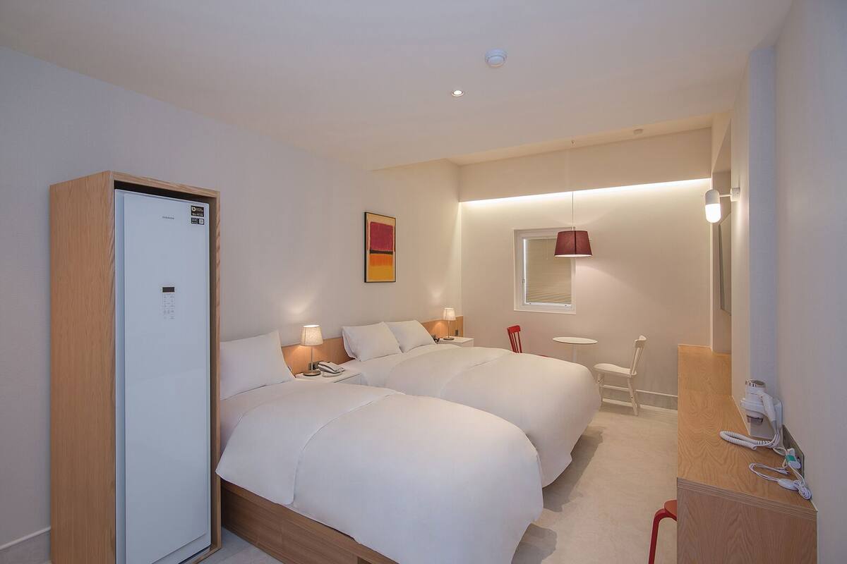 Habitación de hotel con dos camas, un minibar, un escritorio con teléfono, una mesita pequeña y una silla.