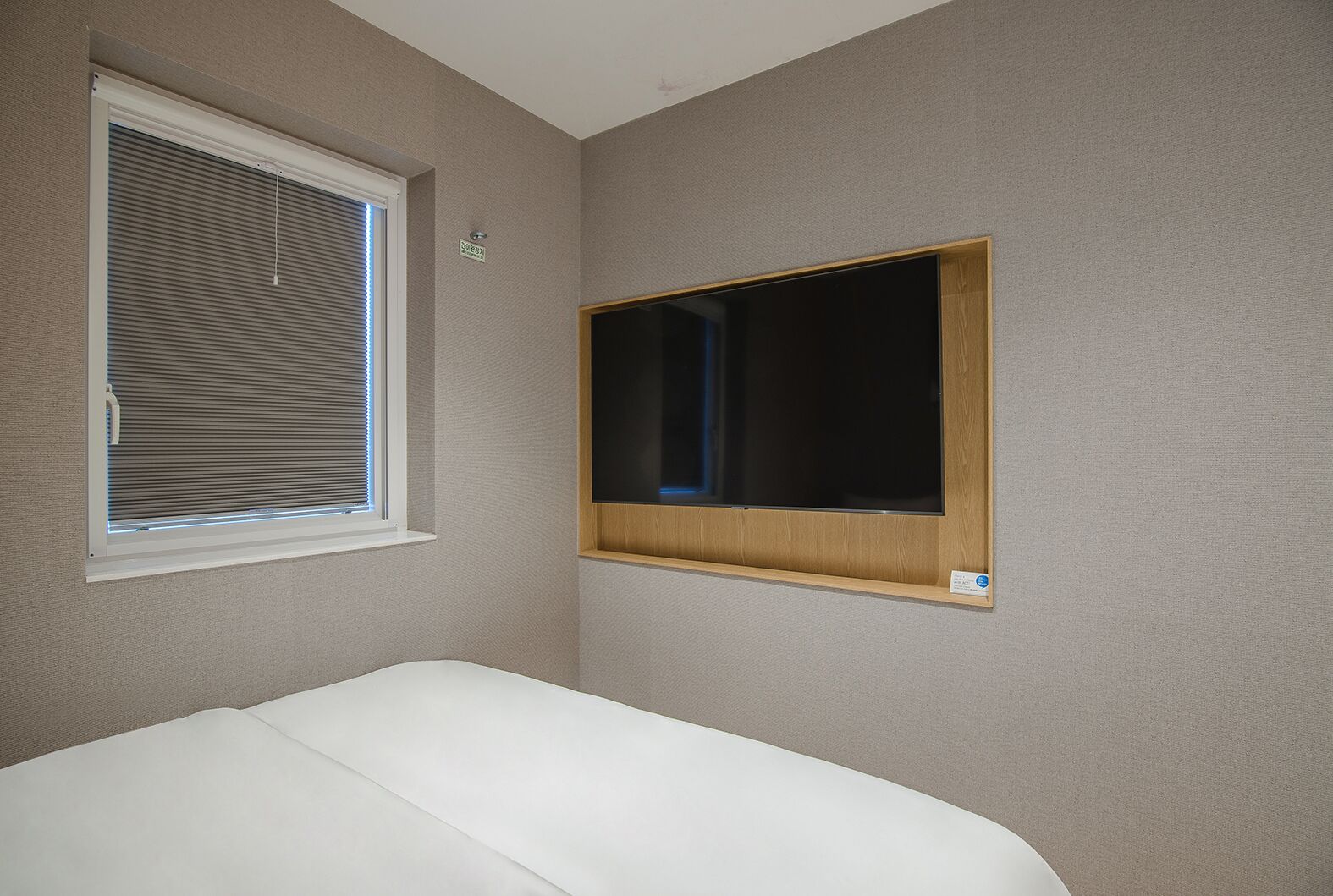 A bedroom with a single bed, a window with blinds, and a mounted TV.