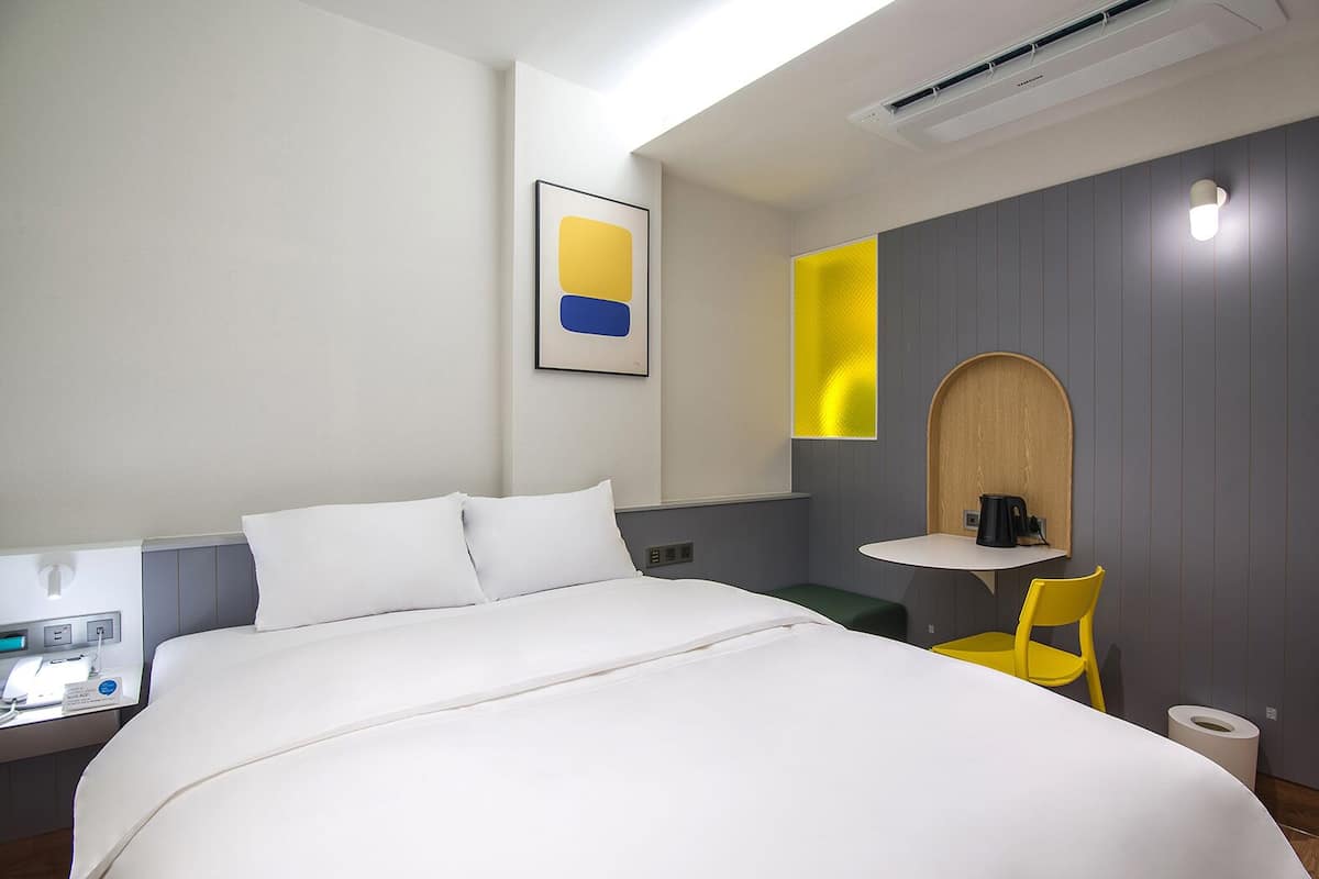 Habitación de hotel con una cama, un escritorio con ordenador, una silla y una mesita con lámpara.