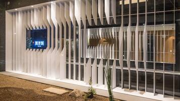 A modern hotel facade with a distinctive white geometric design, a digital signboard, and a gravel pathway with potted plants.