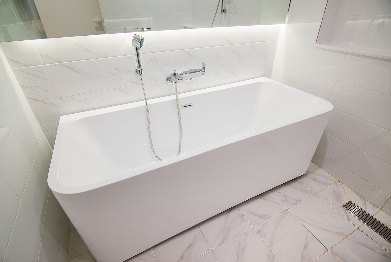A modern bathroom with a white freestanding bathtub, a handheld showerhead, and a wall-mounted faucet.