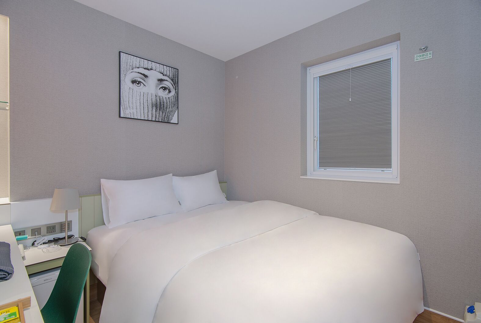 Una habitación de hotel con cama, escritorio con lámpara, silla y ventana con persianas.