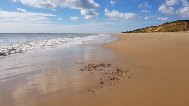 A wide sandy beach with gentle waves and a clear blue sky with scattered clouds. - 5 Sea View Walk - comfortable family home right on the beach, free parking, pets (Pakefield)