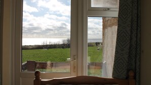A room with a large window overlooking a grassy field and a body of water. - 5 Sea View Walk - comfortable family home right on the beach, free parking, pets (Pakefield)