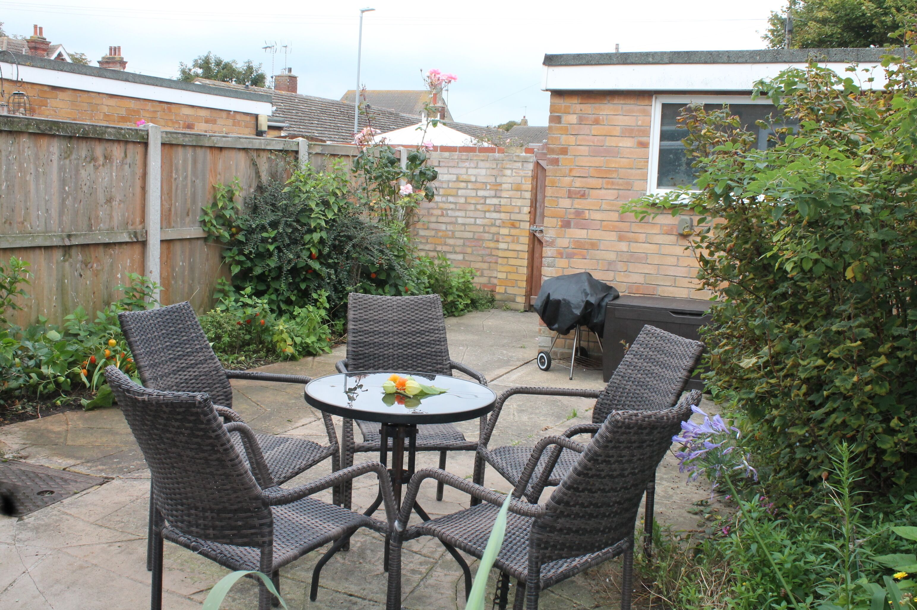A patio with wicker chairs and a table, surrounded by a brick wall and greenery.