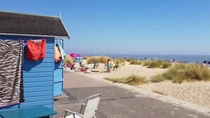 A beachside building with a blue exterior, a chair, and a small table. - 5 Sea View Walk - comfortable family home right on the beach, free parking, pets (Pakefield)