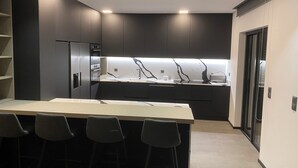 A modern kitchen with dark cabinetry, a central island with bar stools, and built-in appliances.