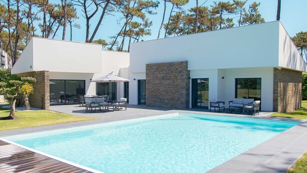 A modern house with a swimming pool, outdoor furniture, and a stone wall.