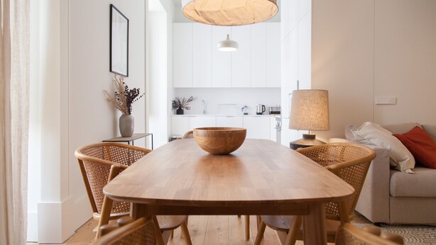 Ein stilvoller Essbereich mit Holztisch und Korbstühlen, einer Pendelleuchte und einer Küche im Hintergrund.