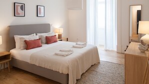 Ein ordentlich eingerichtetes Schlafzimmer mit Bett, Nachttischen, einem Spiegel und einem Fenster mit Vorhängen.
