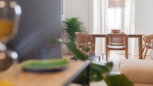 Ein modernes Wohnzimmer mit Essbereich, ausgestattet mit einem großen Fenster, einer Hängelampe und einem Topfpflanzen.