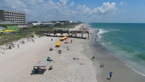 A beach with a pier, sandy shore, and buildings in the background.
