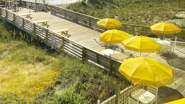 A wooden deck with yellow umbrellas and white chairs overlooking the beach.