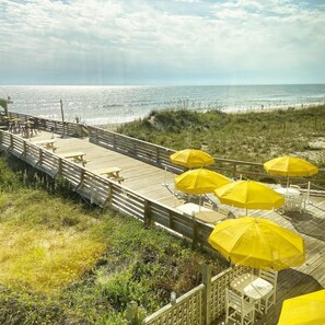 A wooden deck with yellow umbrellas and white chairs overlooking the beach.