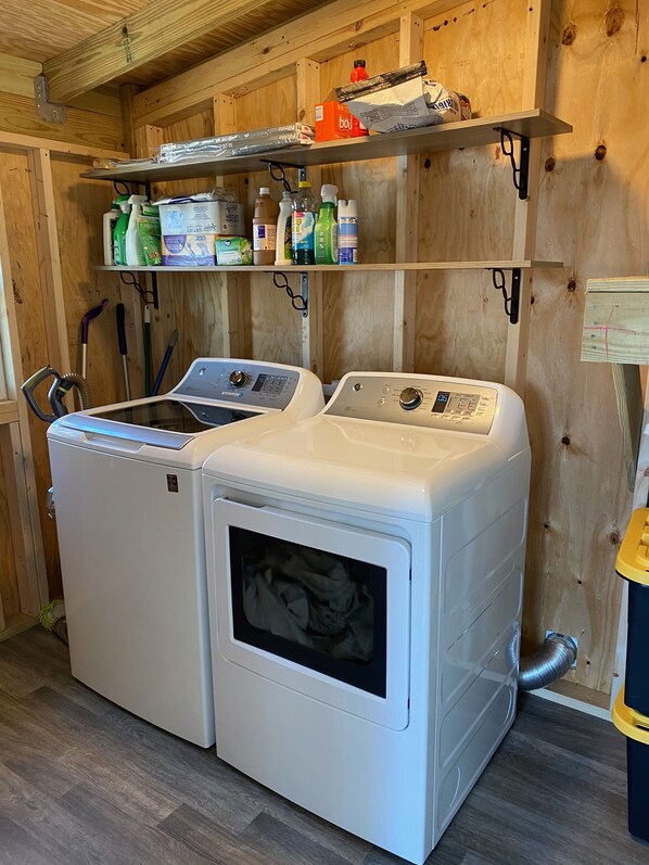 A laundry room with two front-loading washing machines and a shelf above containing cleaning supplies.